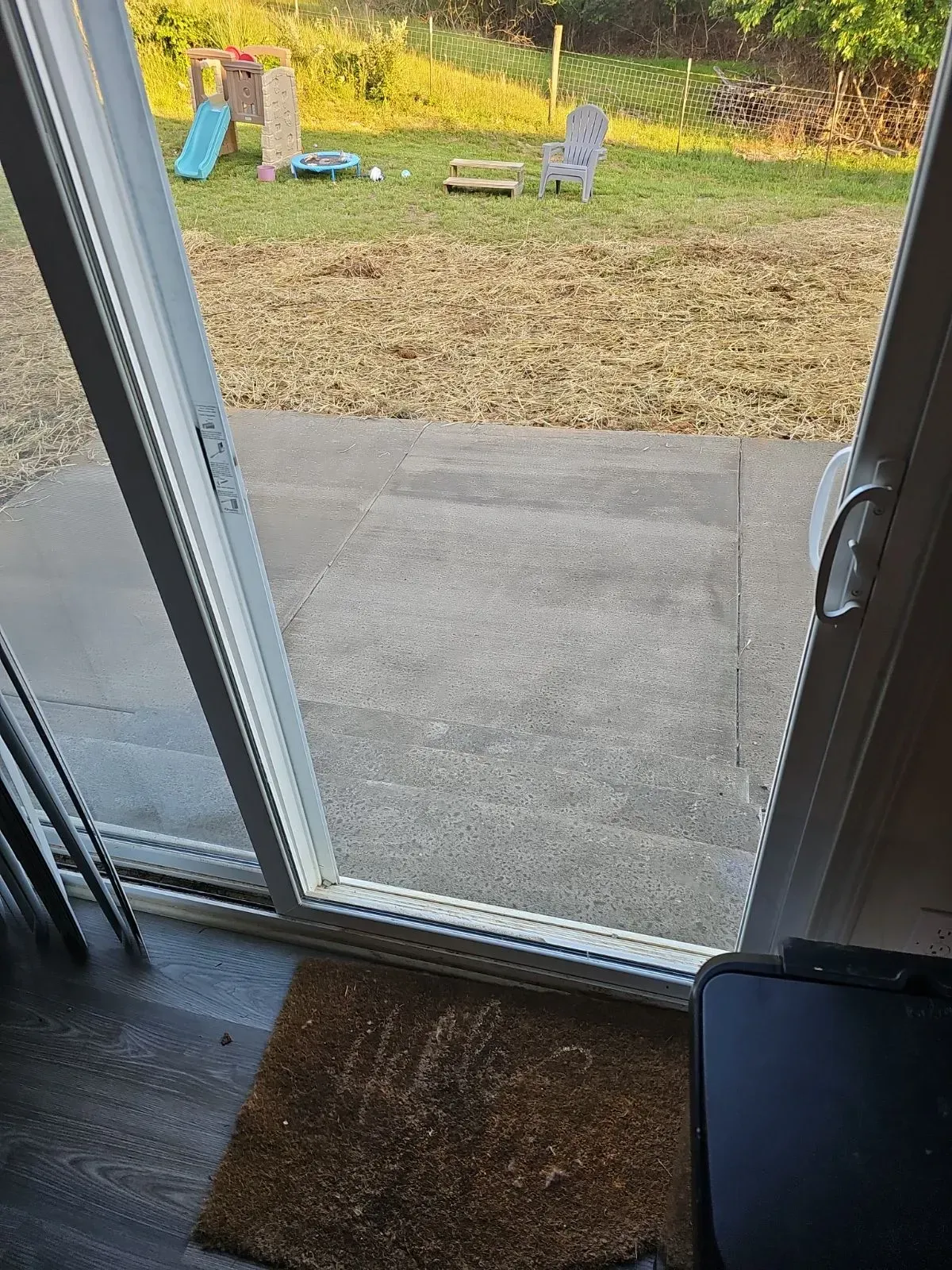 Patio door open to a backyard with grass clippings. A doormat sits inside.