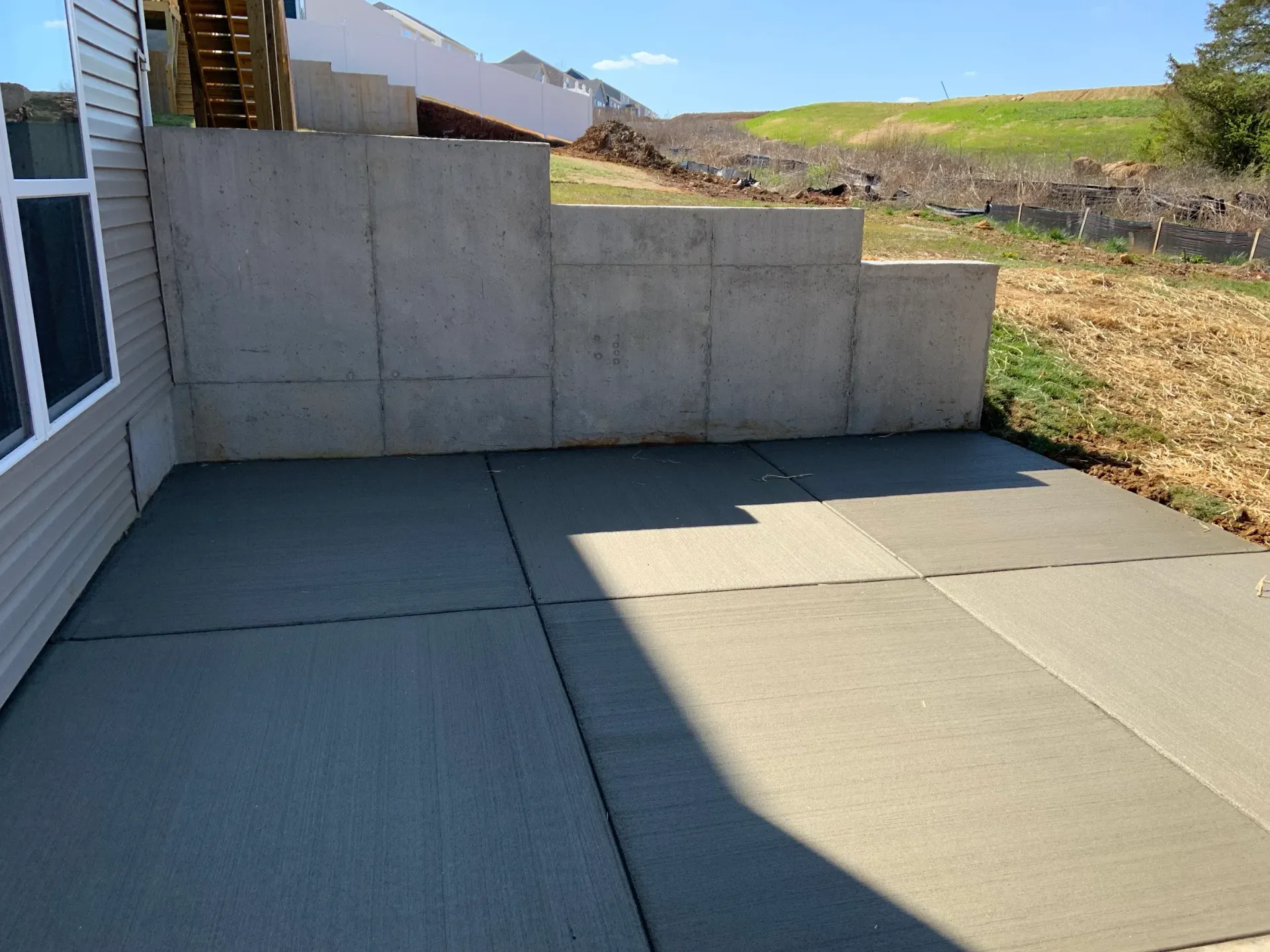 Concrete patio with retaining wall and a sloped backyard on a sunny day.