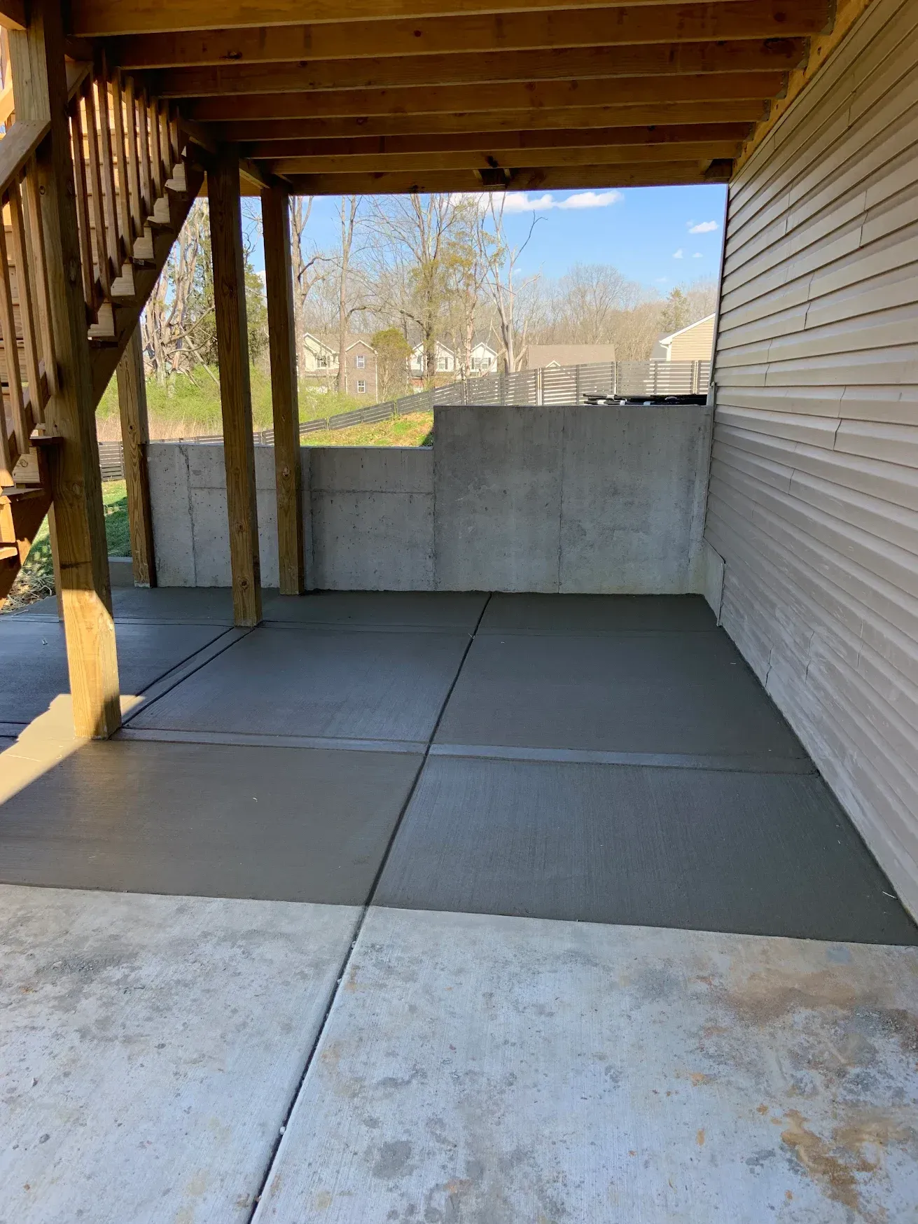 Freshly poured concrete patio beneath a wooden deck, next to a house with siding.