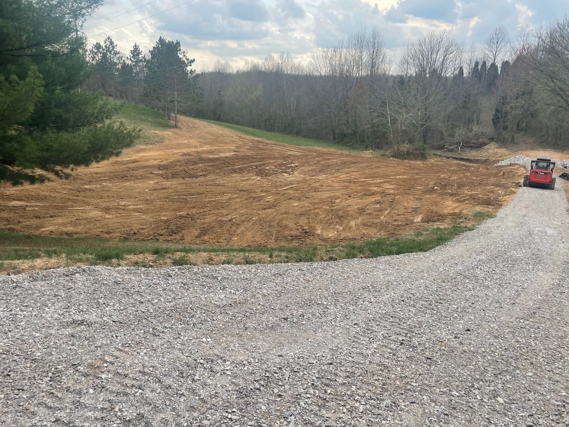 A gravel road going through a field with a bulldozer in the background.