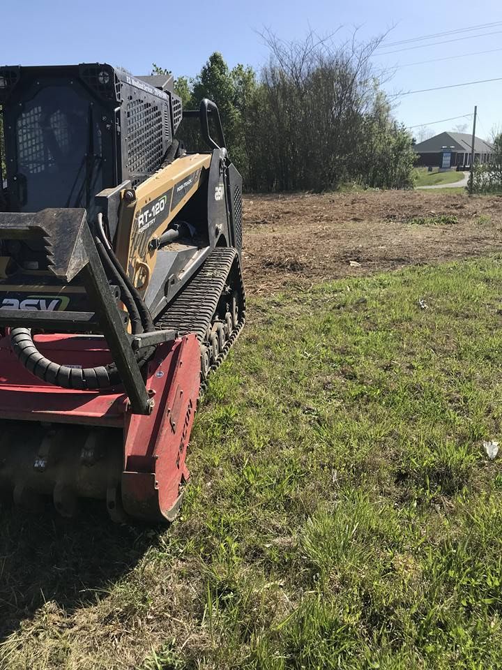 A red tractor is cutting down trees in the woods.