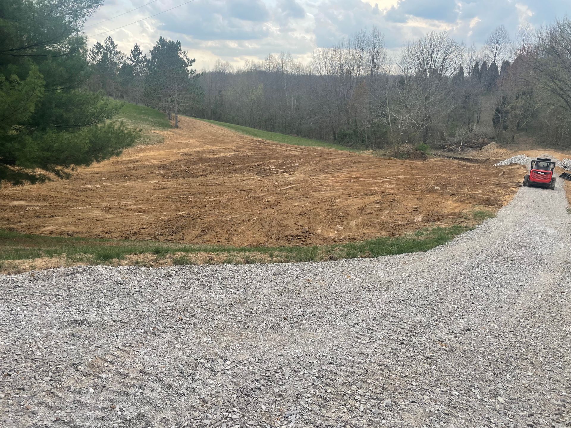 A red truck is driving down a gravel road next to a field.