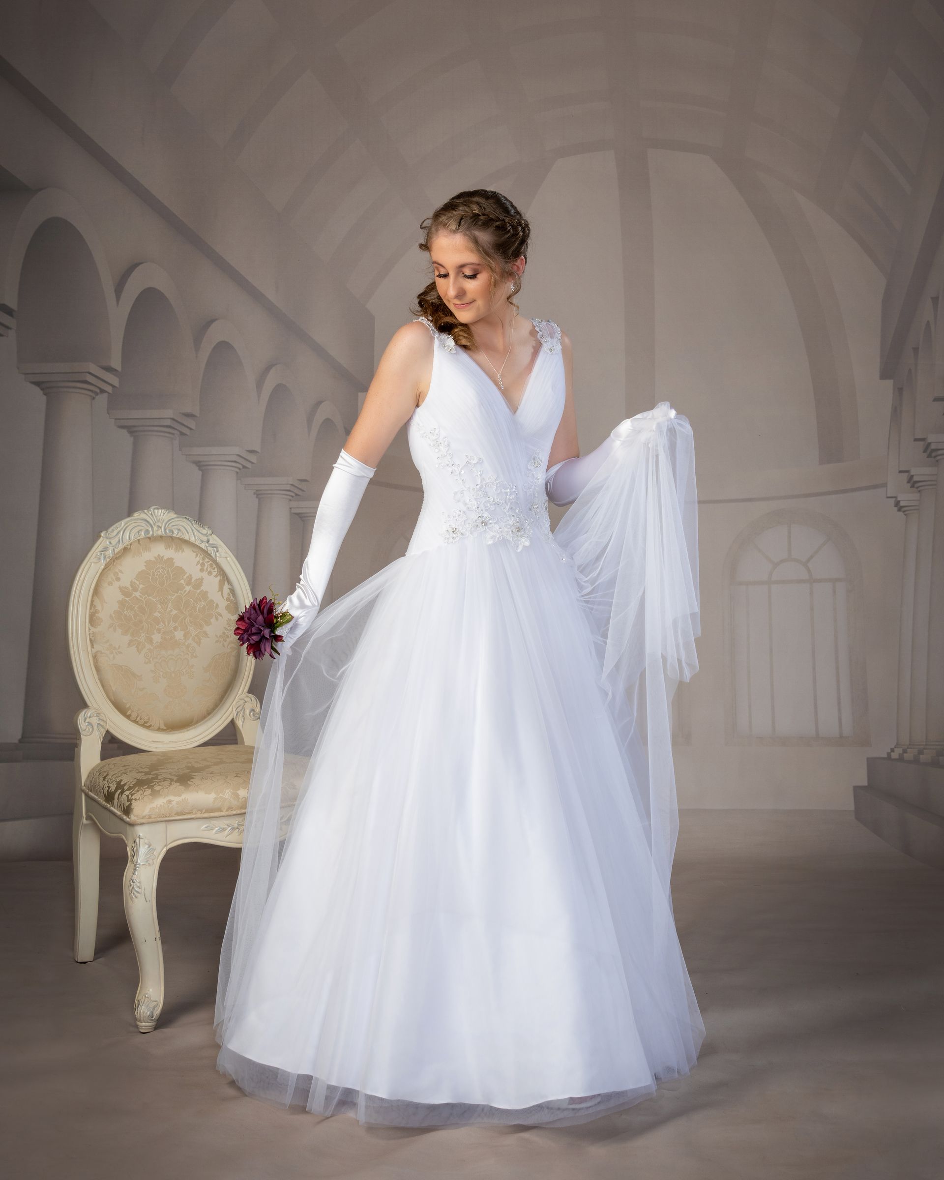 A Woman in a White Dress is Standing in Front of a Chair — Dale Wright Portrait Maker in Shepparton, VIC