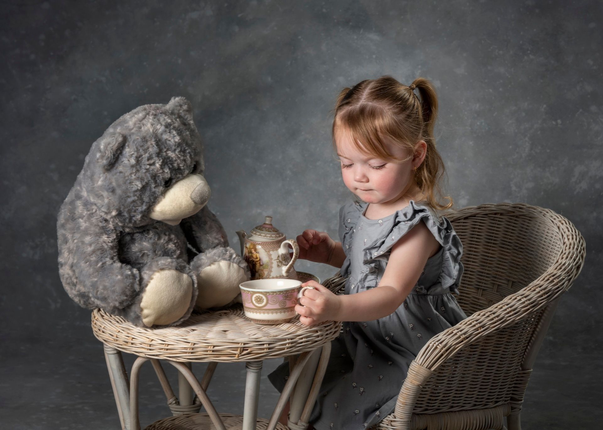 A Little Girl is Sitting at a Table With a Teddy Bear and a Cup of Tea — Dale Wright Portrait Maker in Wangaratta, VIC