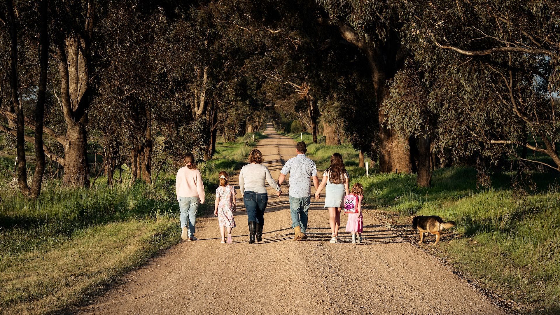 Family of five walking on a dirt path under trees, holding hands with a dog  — Dale Wright Portrait Maker in Shepparton, VIC