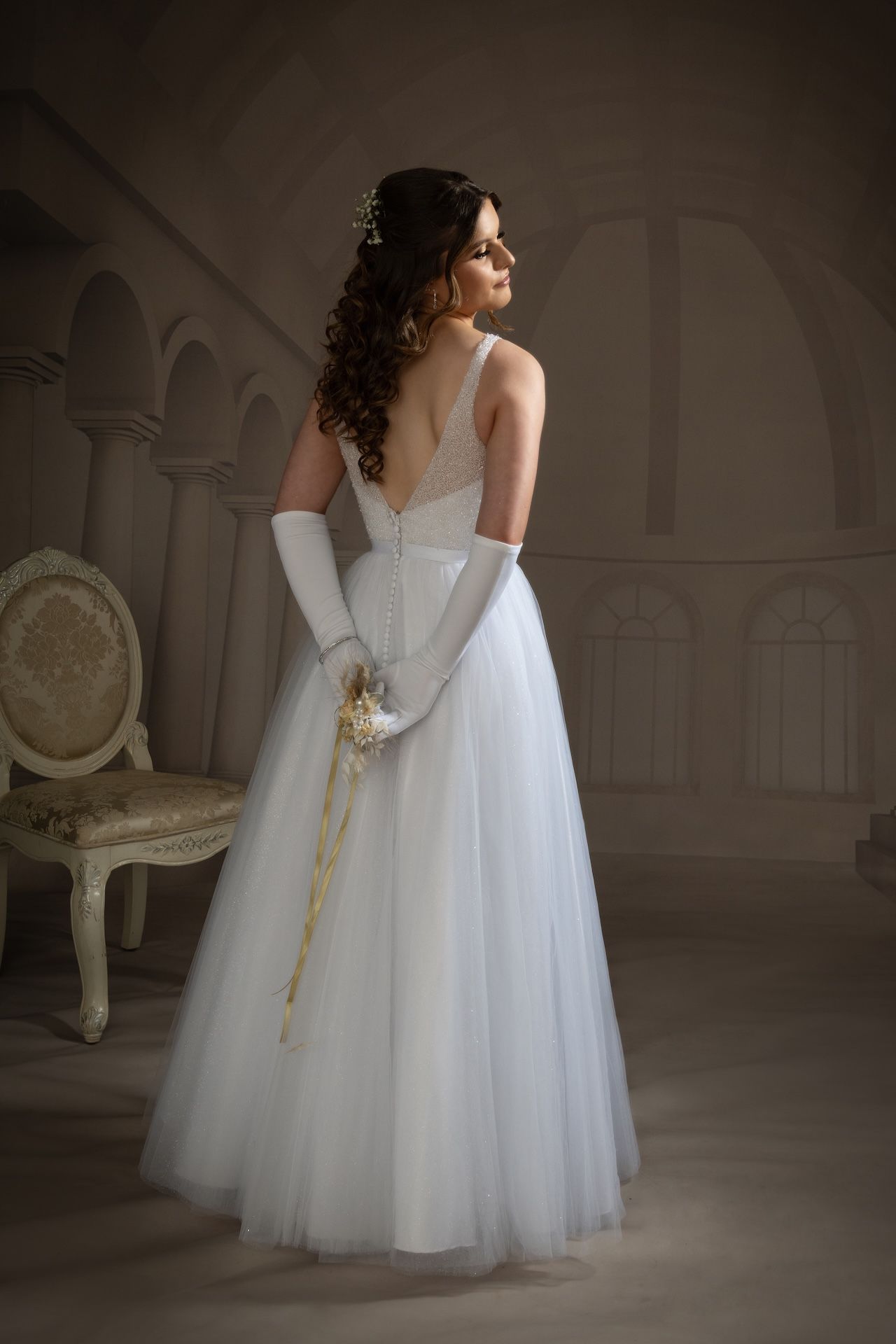 A Woman in a White Dress and White Gloves is Standing Next to a Chair — Dale Wright Portrait Maker in Shepparton, VIC