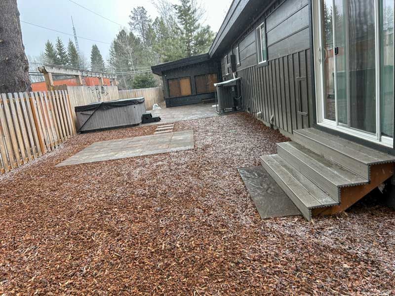 Backyard with a hot tub, steps, and wood chip ground cover. Gray siding and fence.