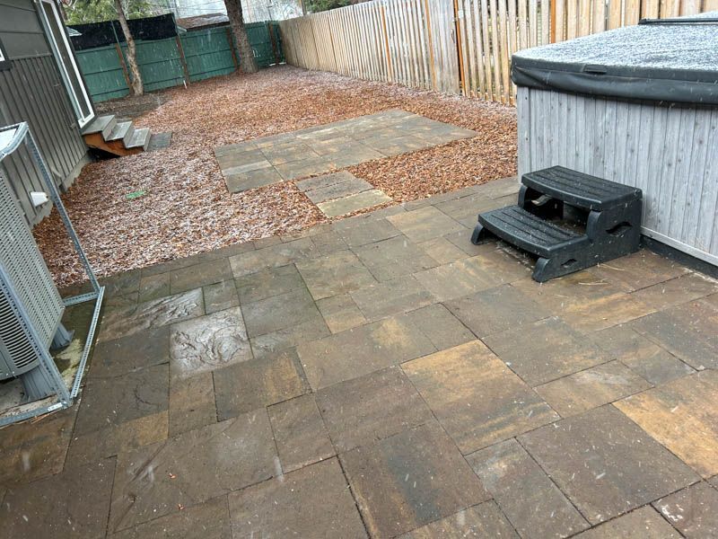 Patio with stone pavers, hot tub with steps, and wood chip pathway.