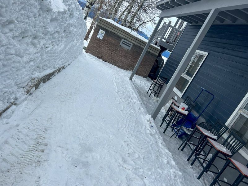 Snowy alleyway next to blue building with outdoor seating, and brick building in background.