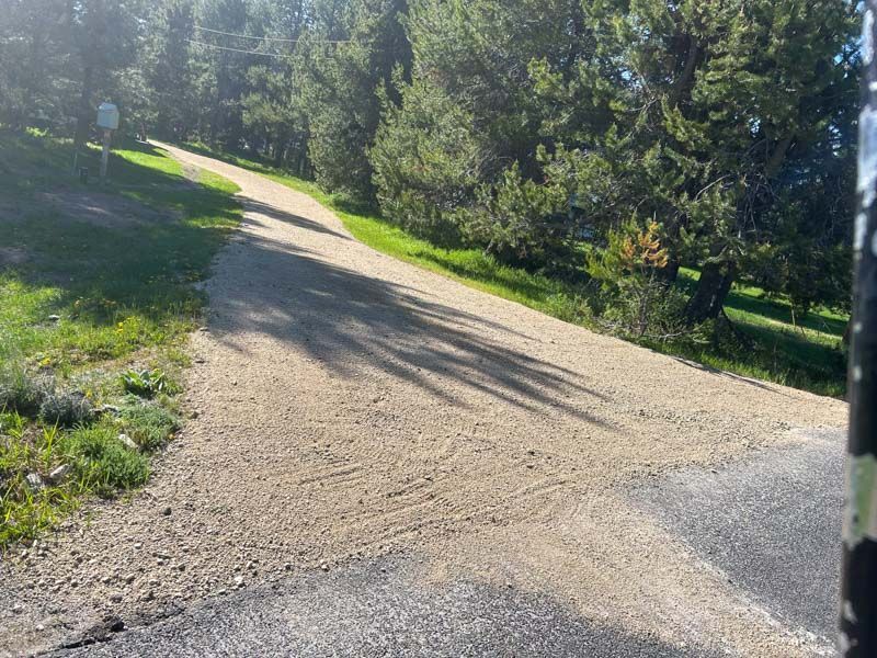 Gravel road forks off paved road, surrounded by grass and trees.