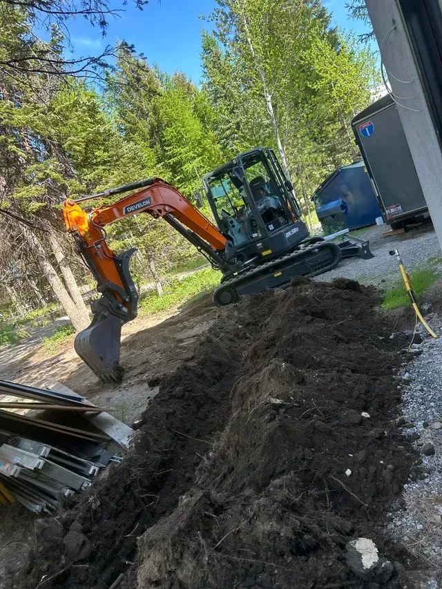 A yellow excavator digging a trench in light brown soil.