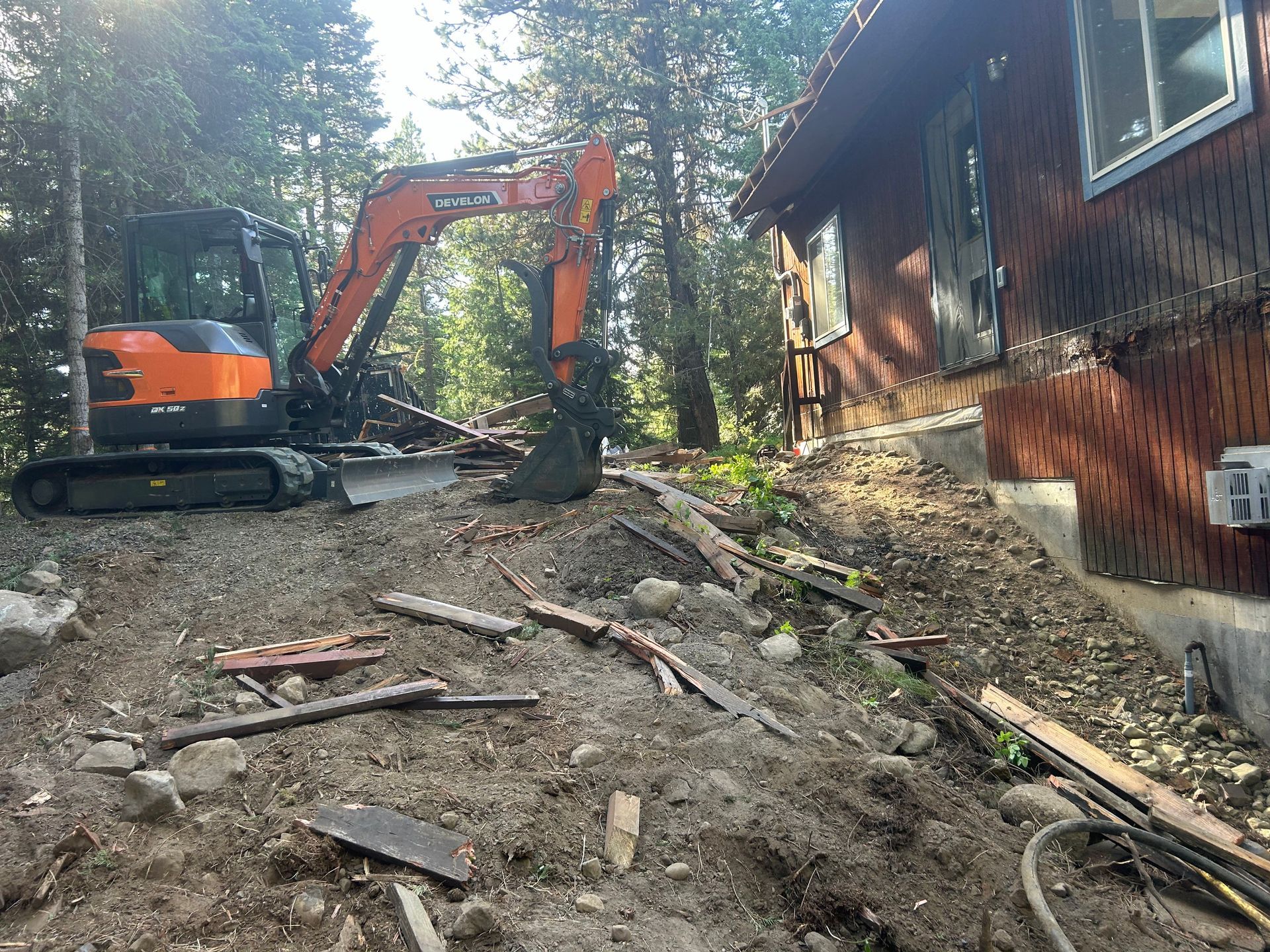 Orange excavator clearing trees in a wooded area with bare trees and debris.