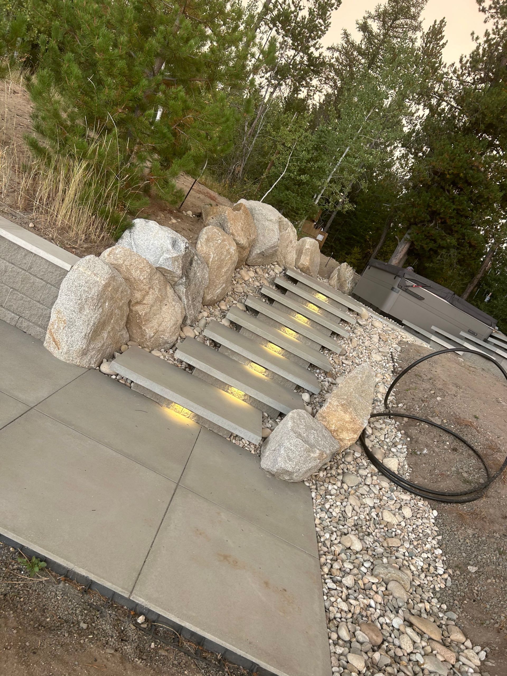 Patio with stone pavers, hot tub with steps, and wood chip pathway.