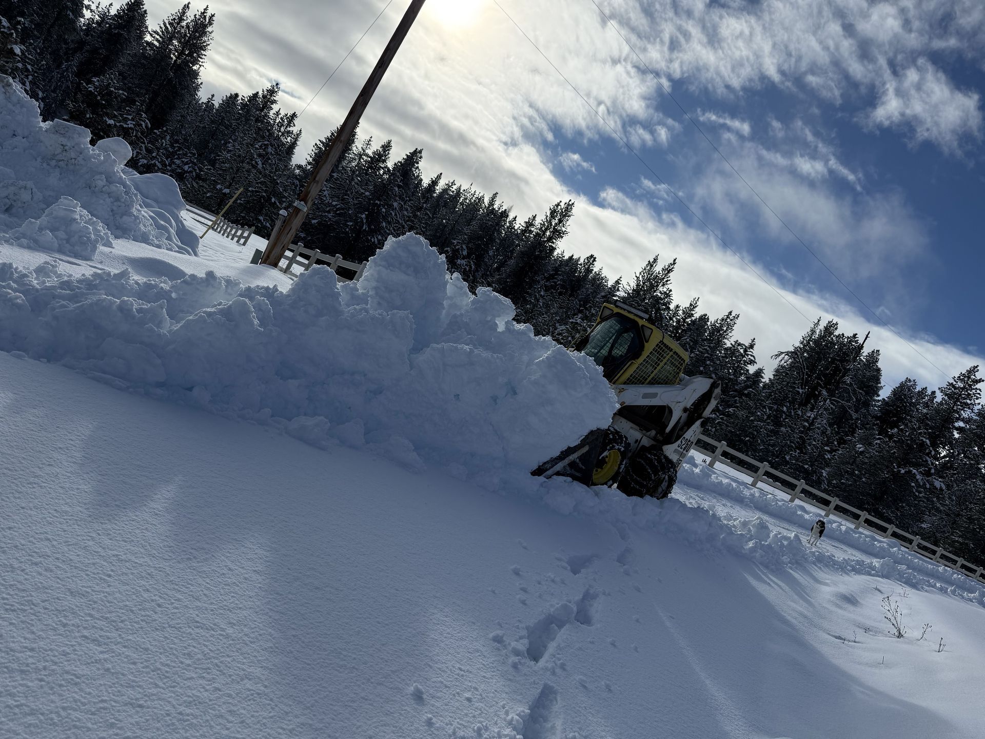 Small snowplow clearing a narrow path next to a building, high snow banks on either side.