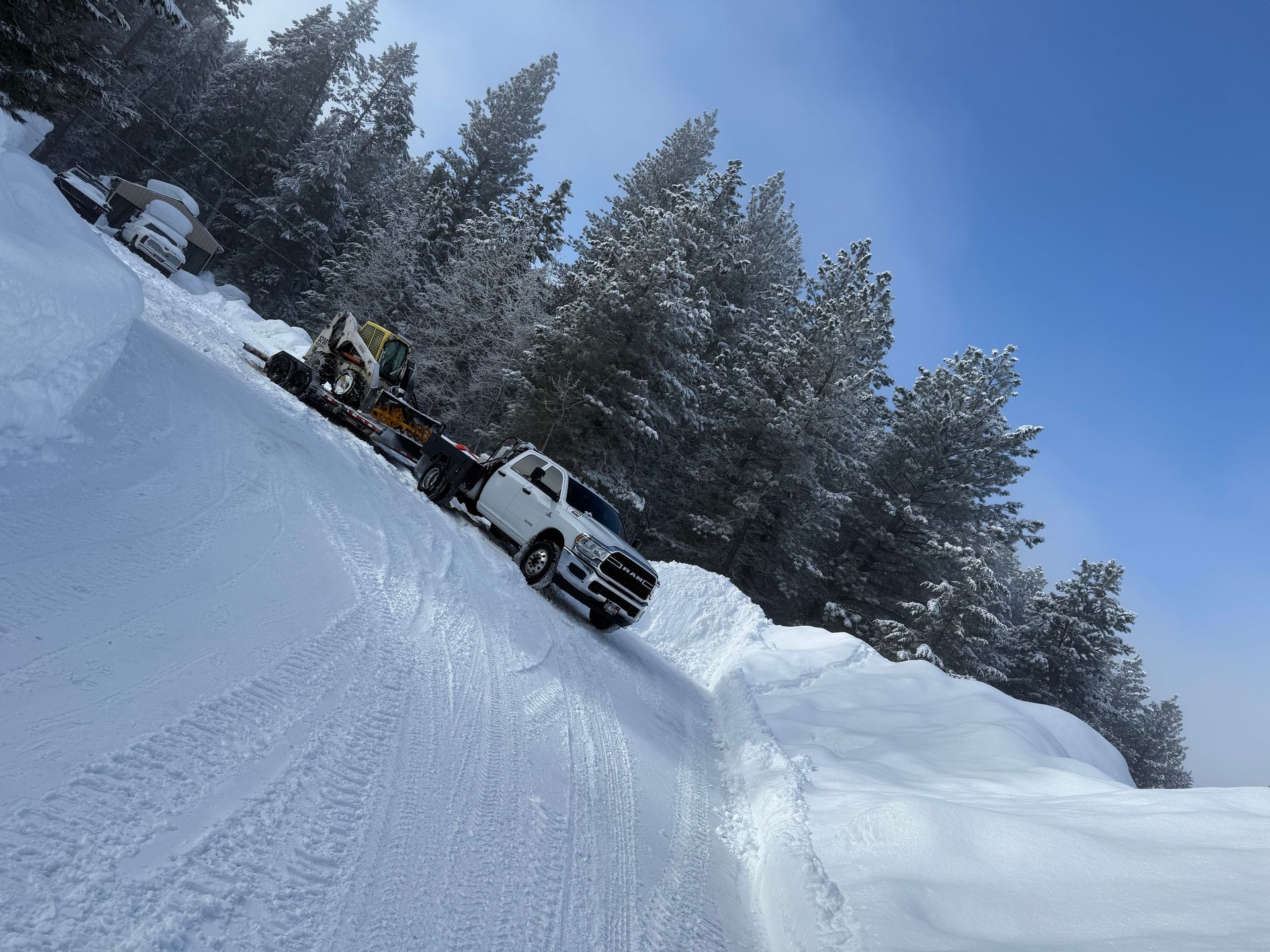 Snow-covered driveway between two wooden buildings, bridge overhead. Snow piled on the right.