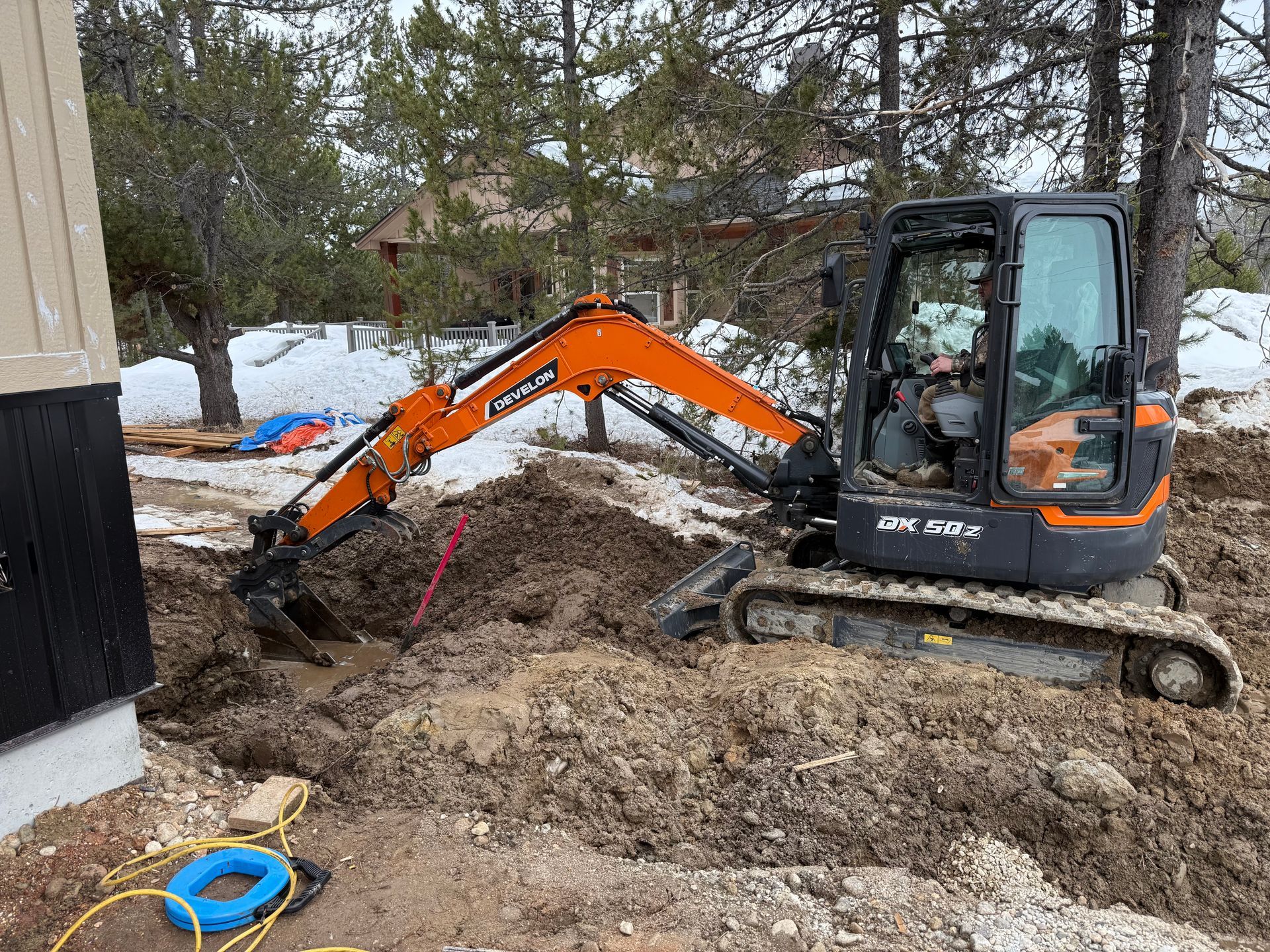 Yellow excavator digging a long trench in brown earth under a blue sky.