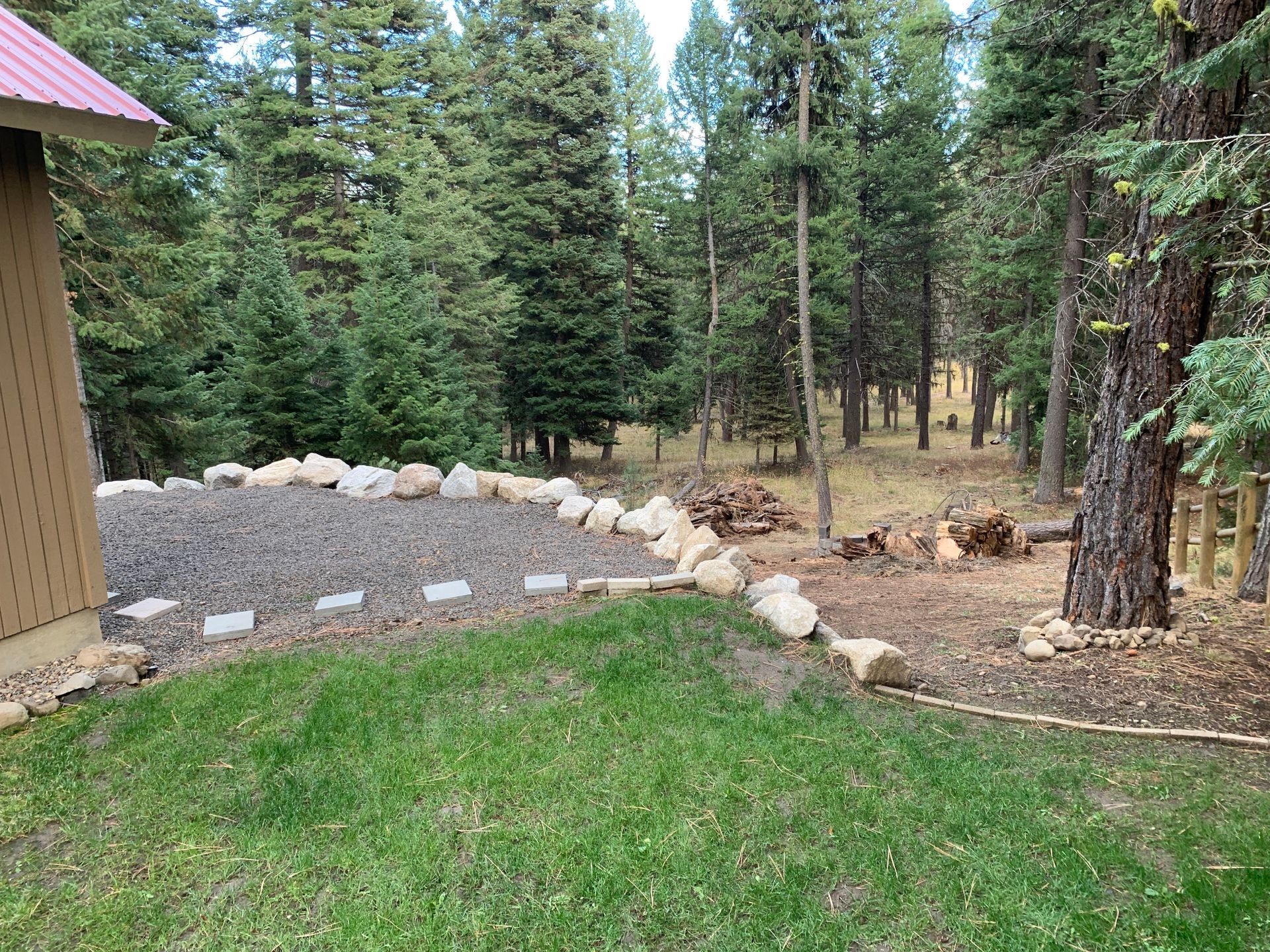 Grassy lawn bordered by rocks and gravel, leading to a wooded area with trees.