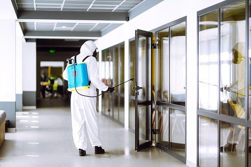 Man in a white suit disinfecting a door in a hallway.