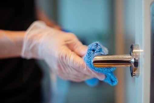 A person wearing gloves sanitizing a door handle for hygiene.