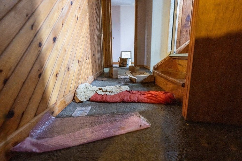 Interior of a house with significant water damage from flooding, showing waterlogged floors and damaged belongings.
