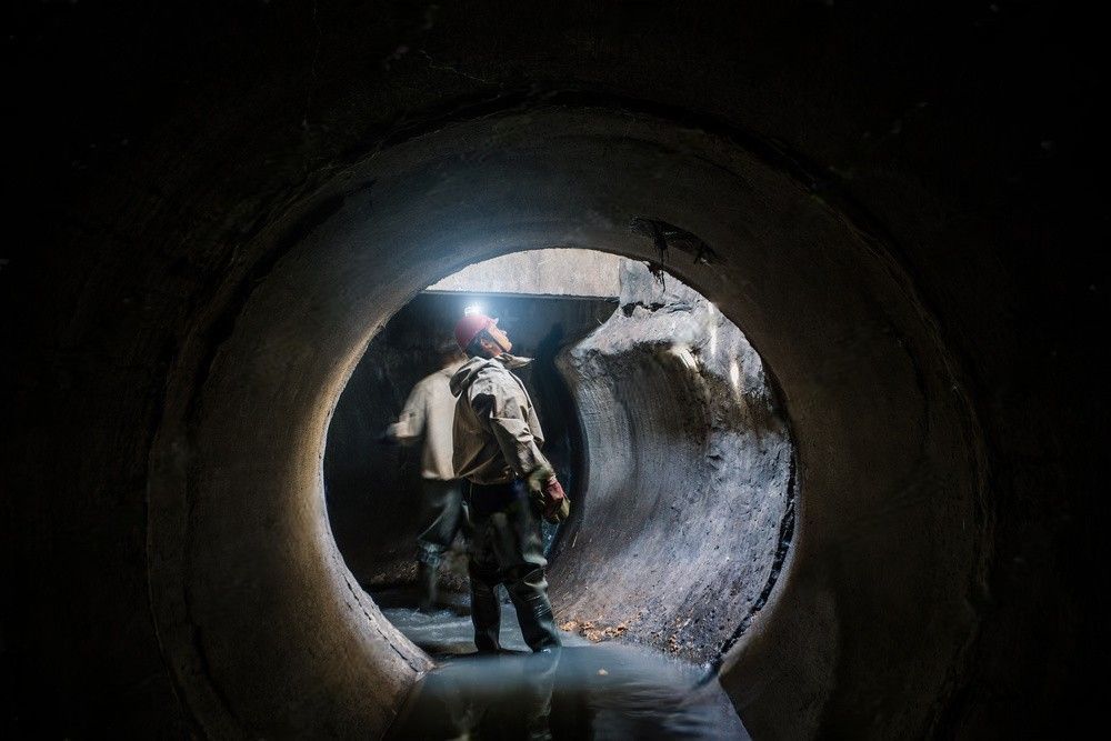 Sewer tunnel worker inspect and document sewer system damage and wastewater leakage.