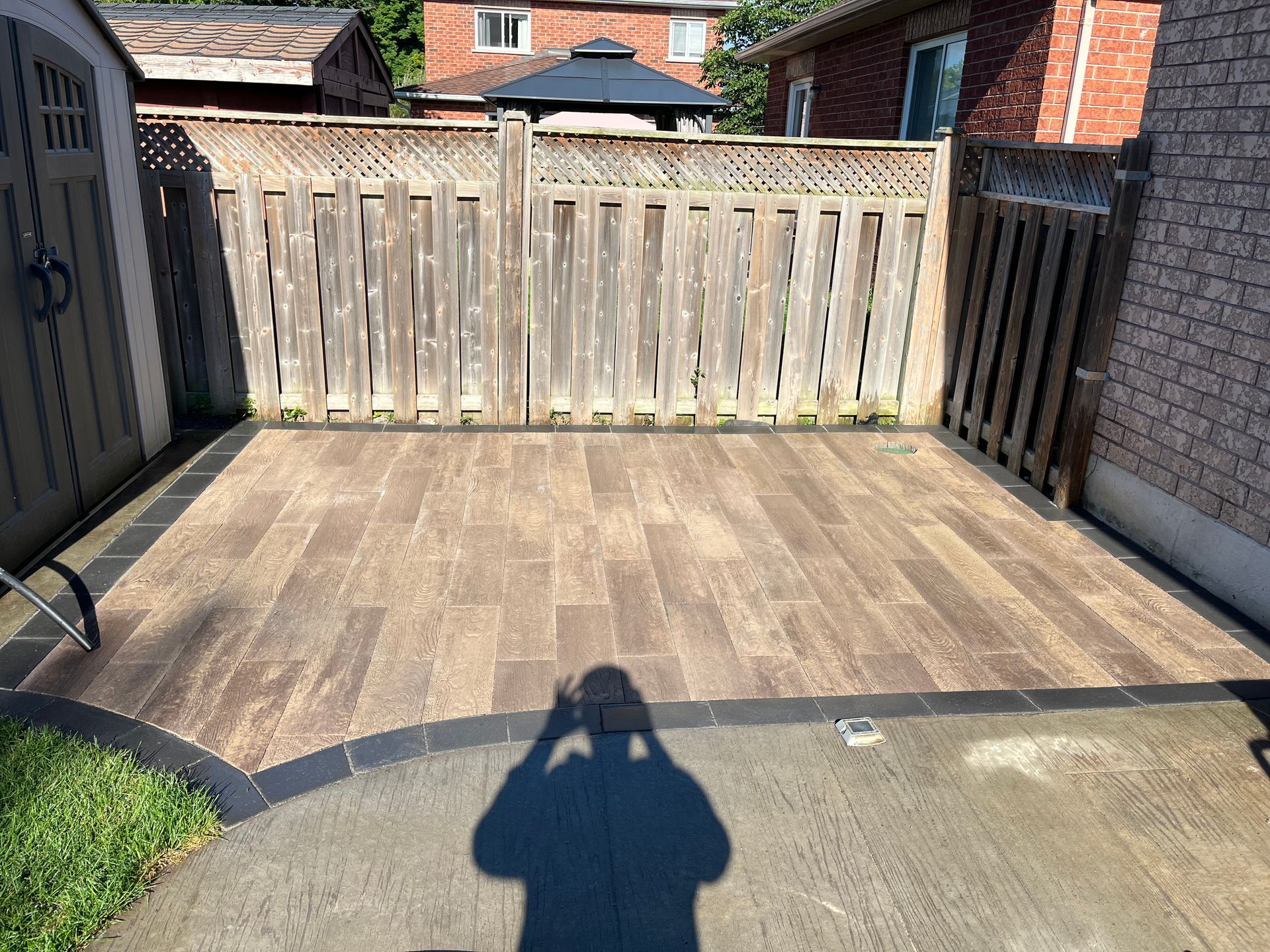 a shadow of a person is cast on a tiled patio in front of a wooden fence .
