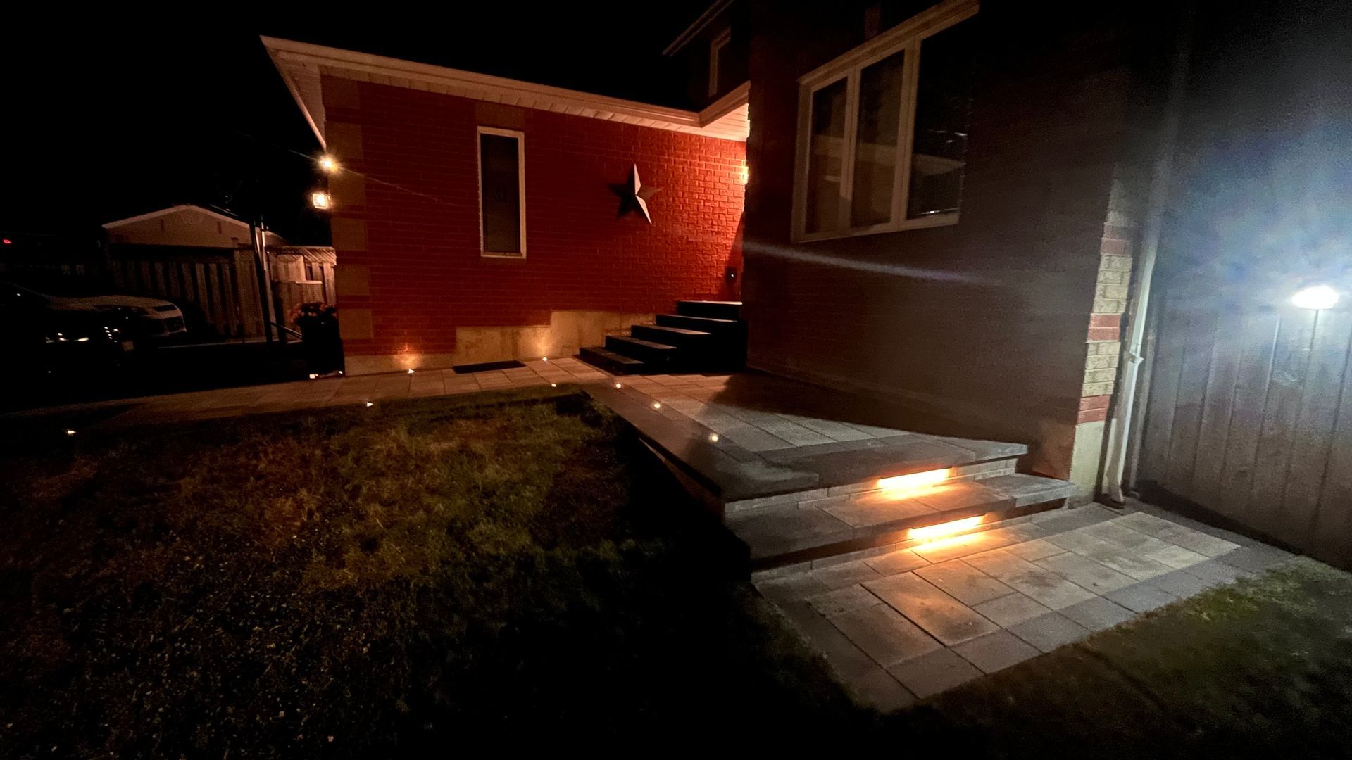 Night view of a red brick house with lit steps and pathway.