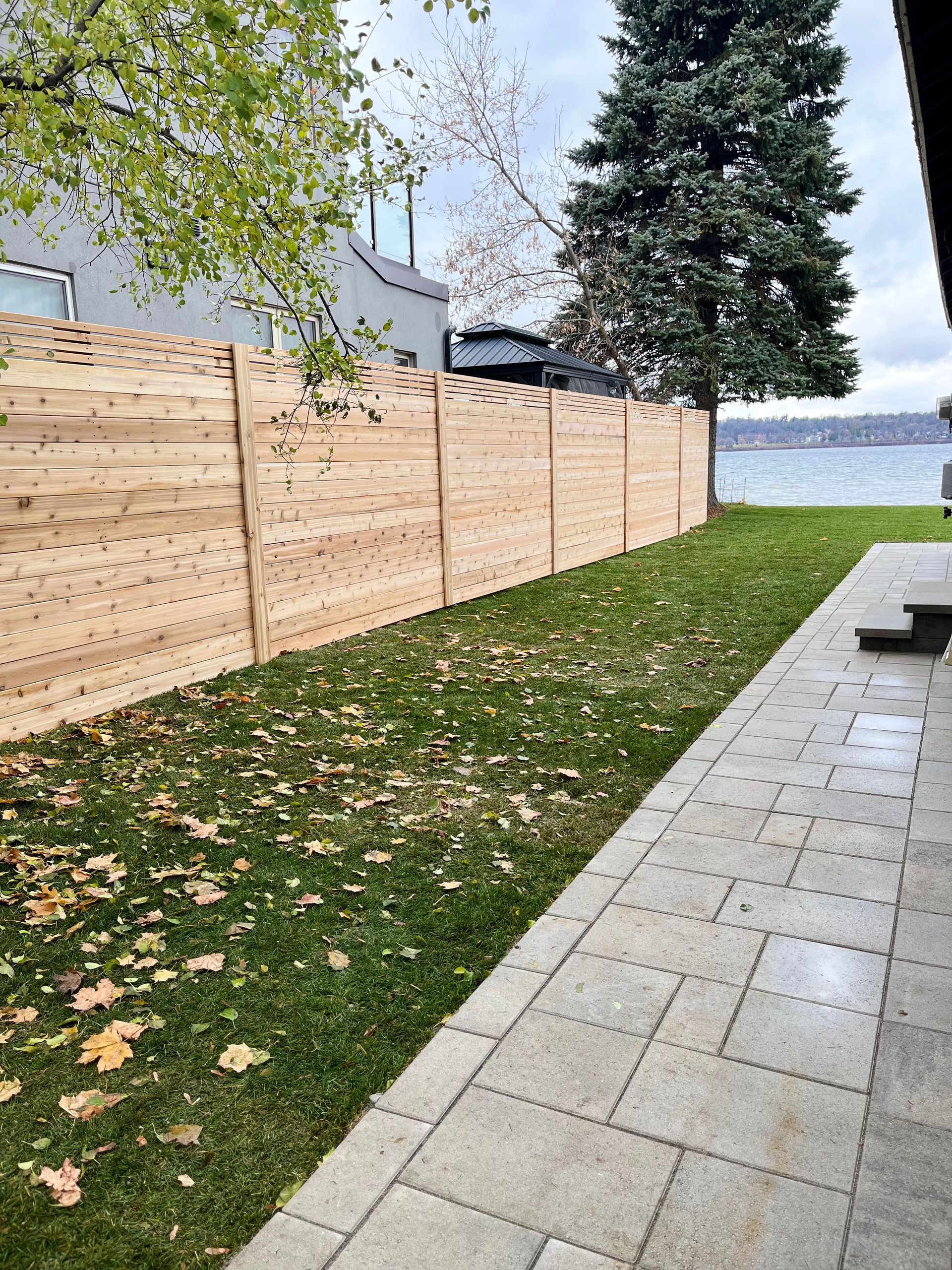 A wooden fence surrounds a lush green yard next to a lake.