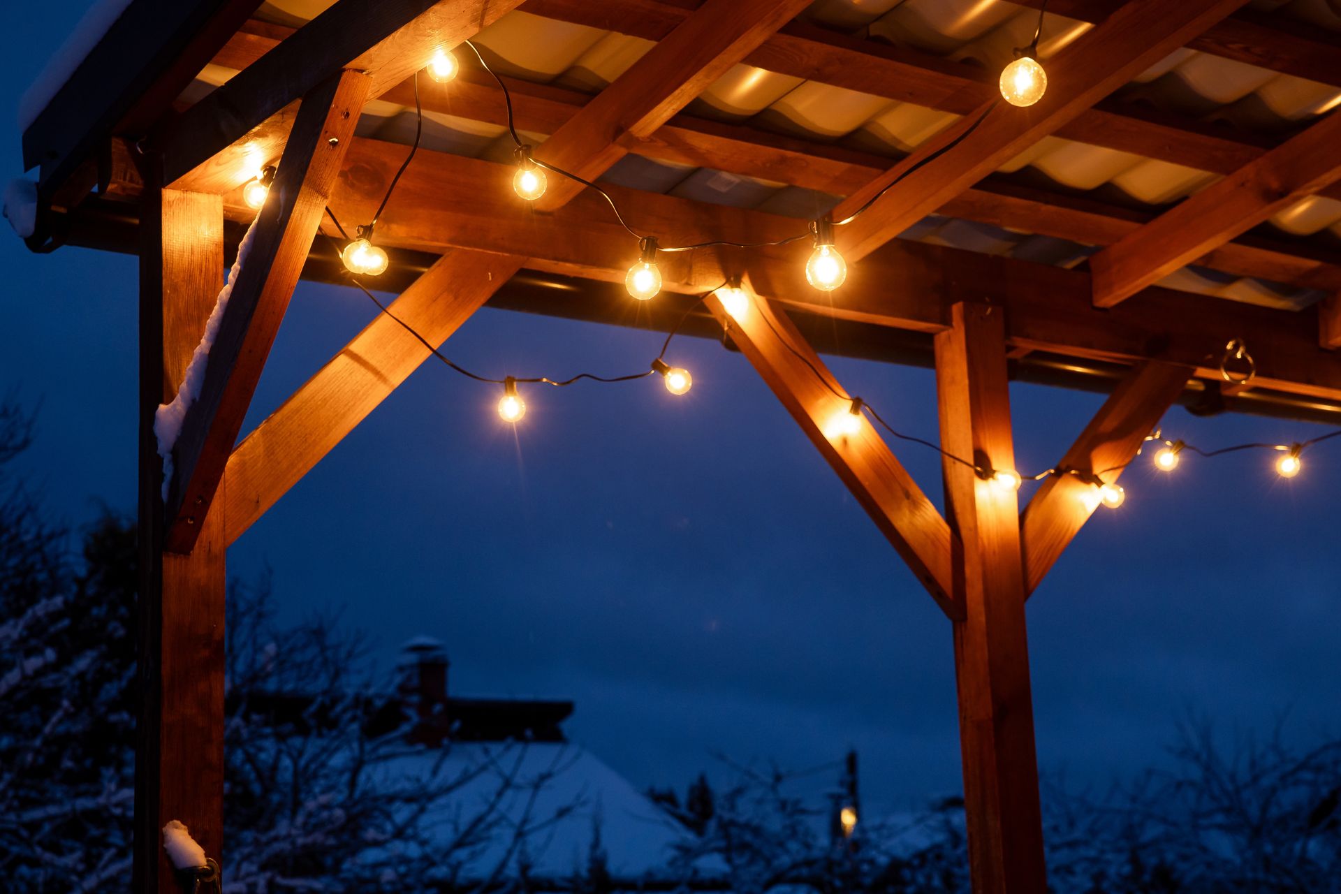 Wooden pergola illuminated by string lights at dusk.