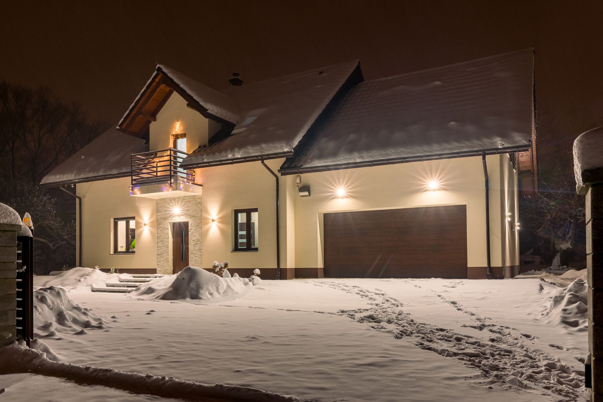 Snowy house at night, illuminated lights, snow-covered roof and yard.