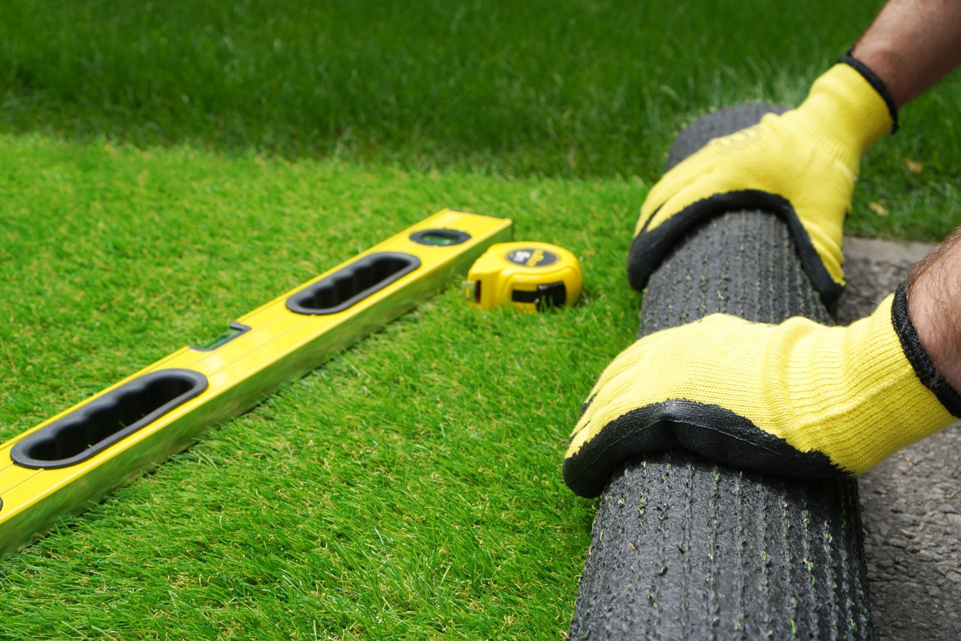 a person wearing yellow gloves is measuring a lawn with a tape measure and a level .