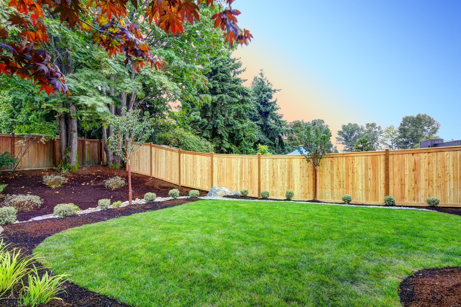 a backyard with a wooden fence and a lush green lawn .