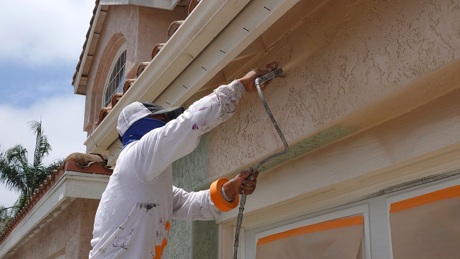 A painting contractor uses a spray paint gun to paint the exterior stucco of a home.