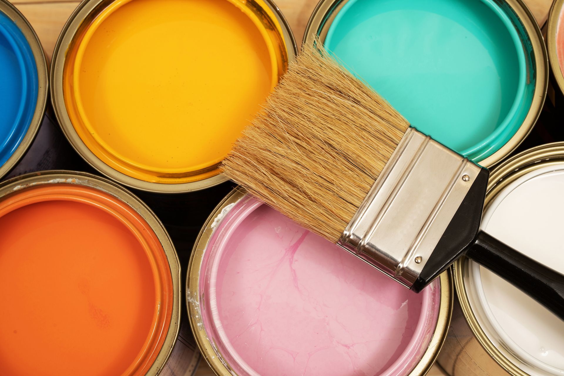 Paint cans in various bright colors, paint brush on top.
