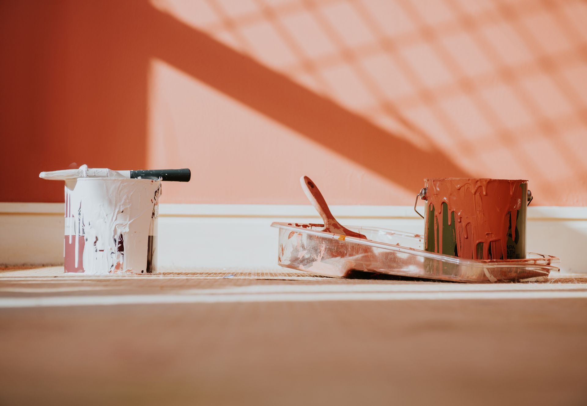 Paint cans and supplies on a floor; a wall is painted coral with shadows.