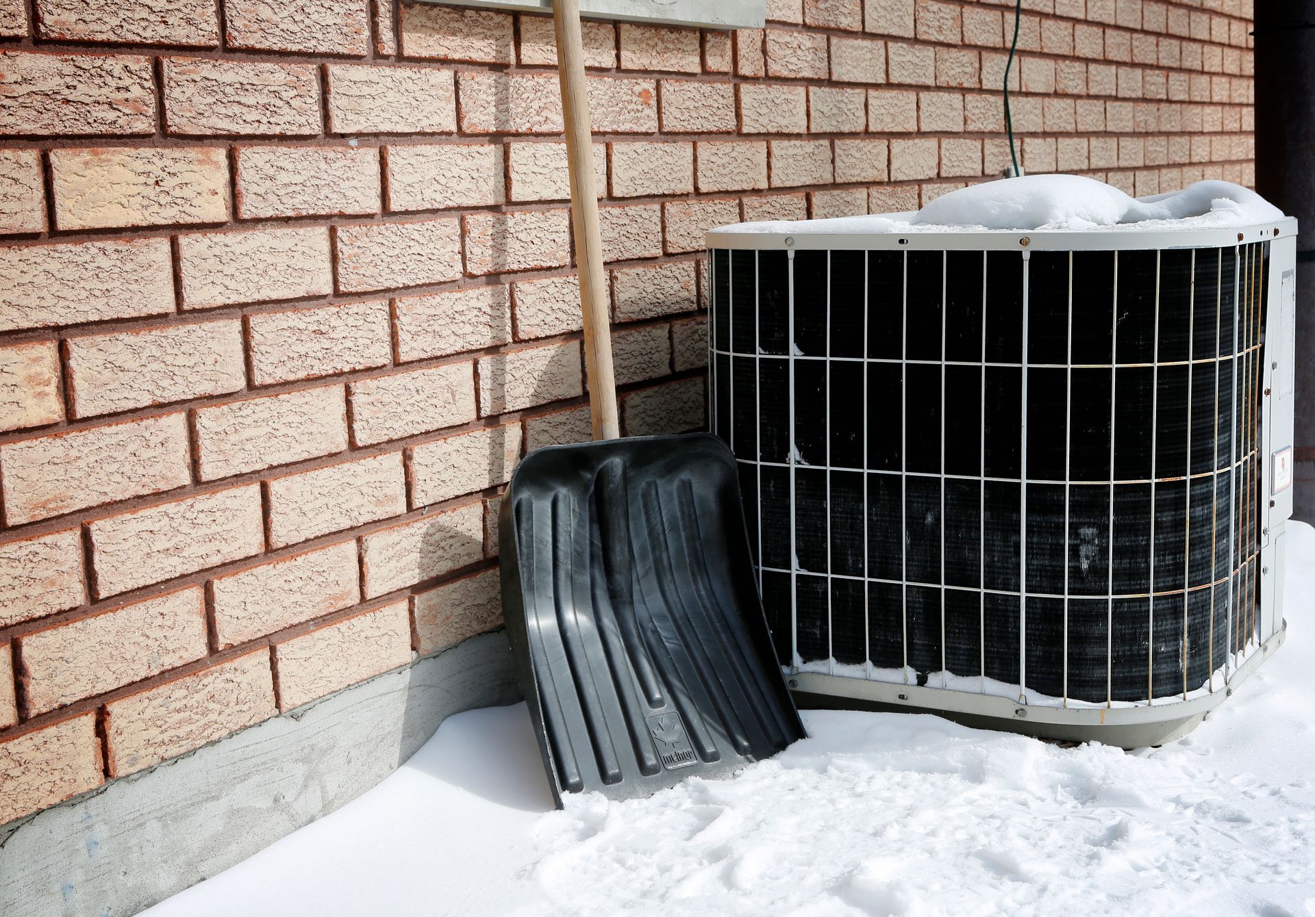 Snow covering and surrounding AC unit outside with snow shuffle next to it.