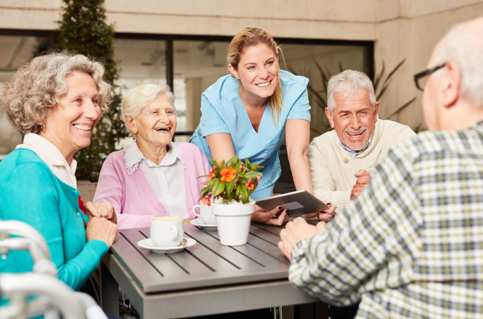 A group of elderly people are sitting around a table with a nurse.