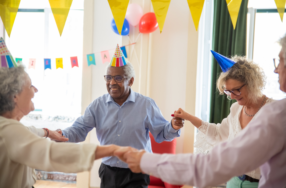 A group of elderly people are dancing in a circle at a birthday party.