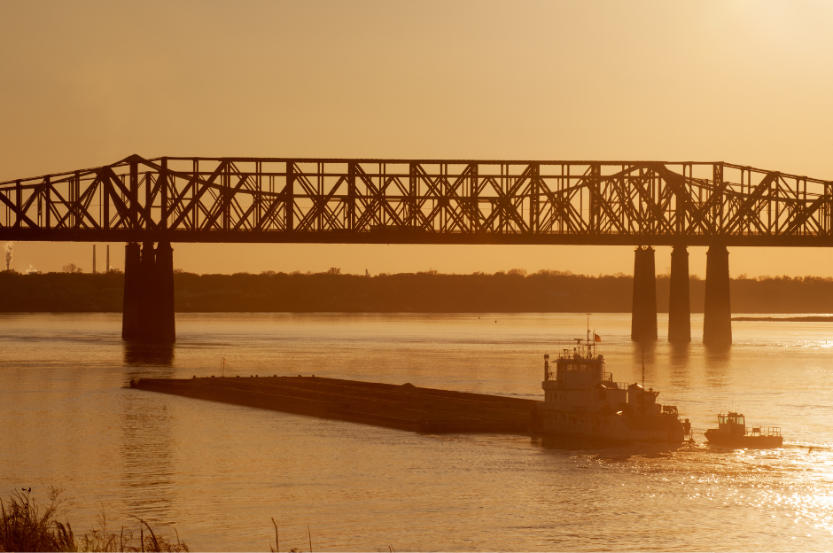 A tugboat is pulling a barge under a bridge over a river.