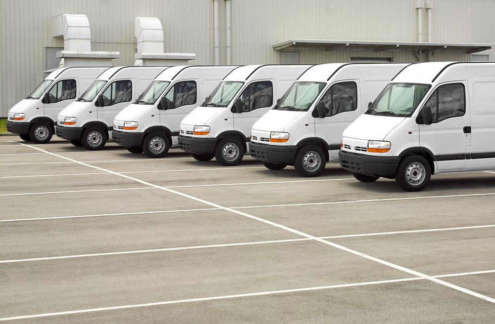 Six White Vans Parked in a Row in a Paved Lot — Dave's Drive U Anywhere 24/7 Mini Van Hire In Wollongong, NSW