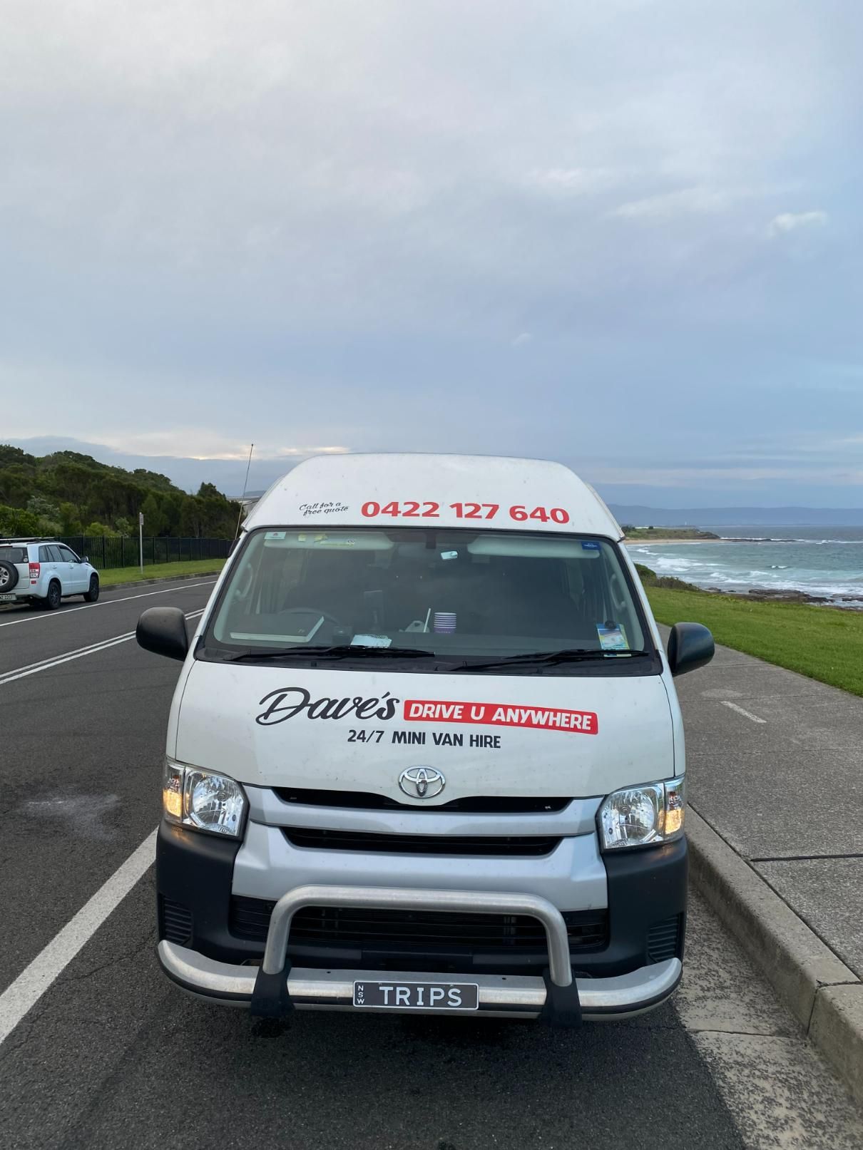 White Van With Dave's Drive U Anywhere Logo, Parked on a Road Next to the Ocean — Dave's Drive U Anywhere 24/7 Mini Van Hire In Albion Park, NSW
