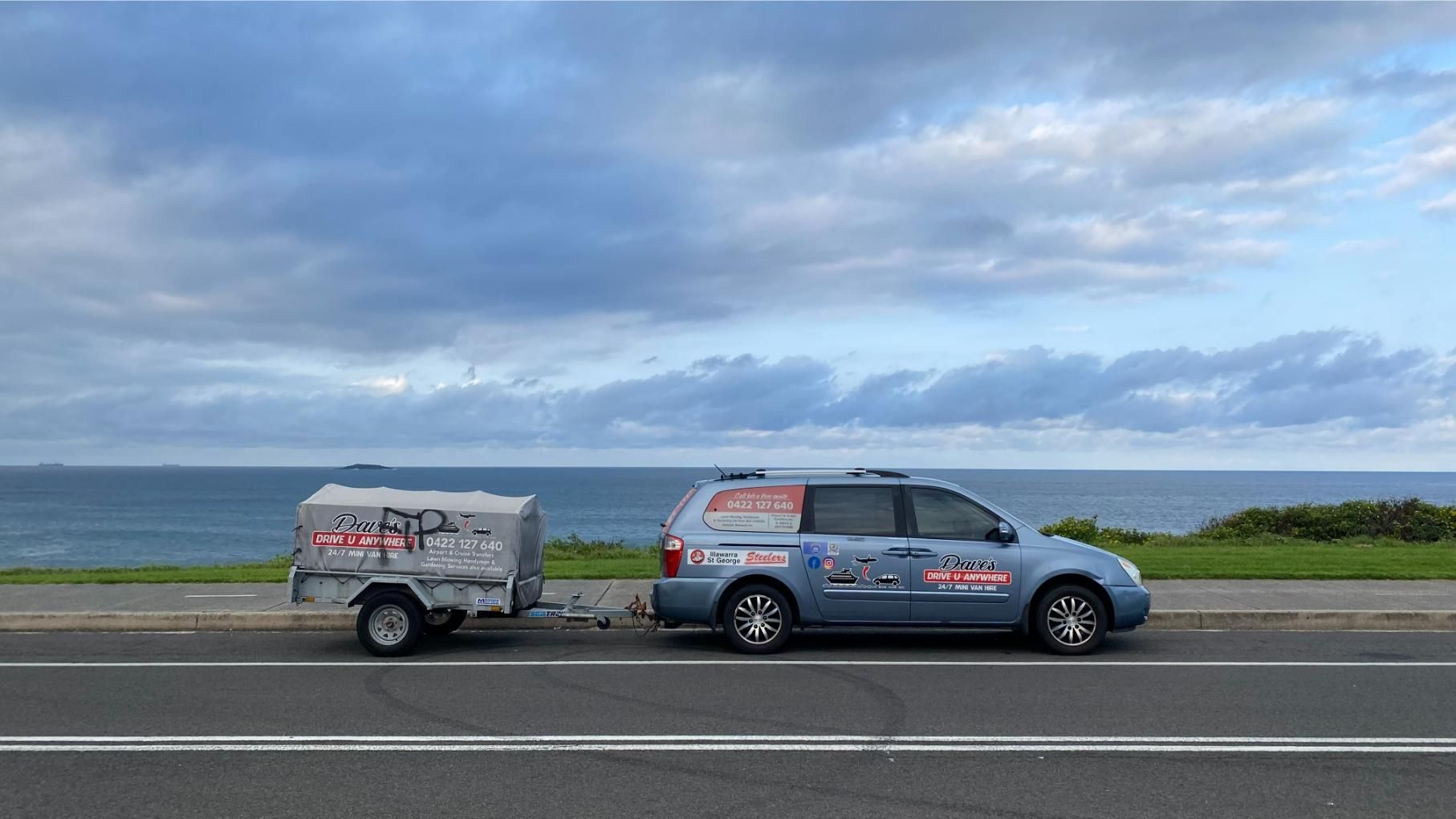 Blue Car Towing a Trailer on a Coastal Road — Dave's Drive U Anywhere 24/7 Mini Van Hire In Albion Park, NSW