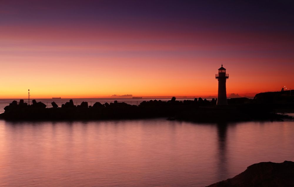 A Lighthouse Is Silhouetted Against a Sunset Over a Body of Water — Daves Drive U Anywhere in Wollongong, NSW