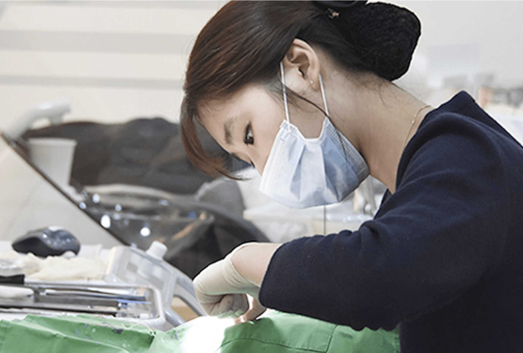 Dentist wearing mask and gloves, focused on patient. Setting is a dental office.