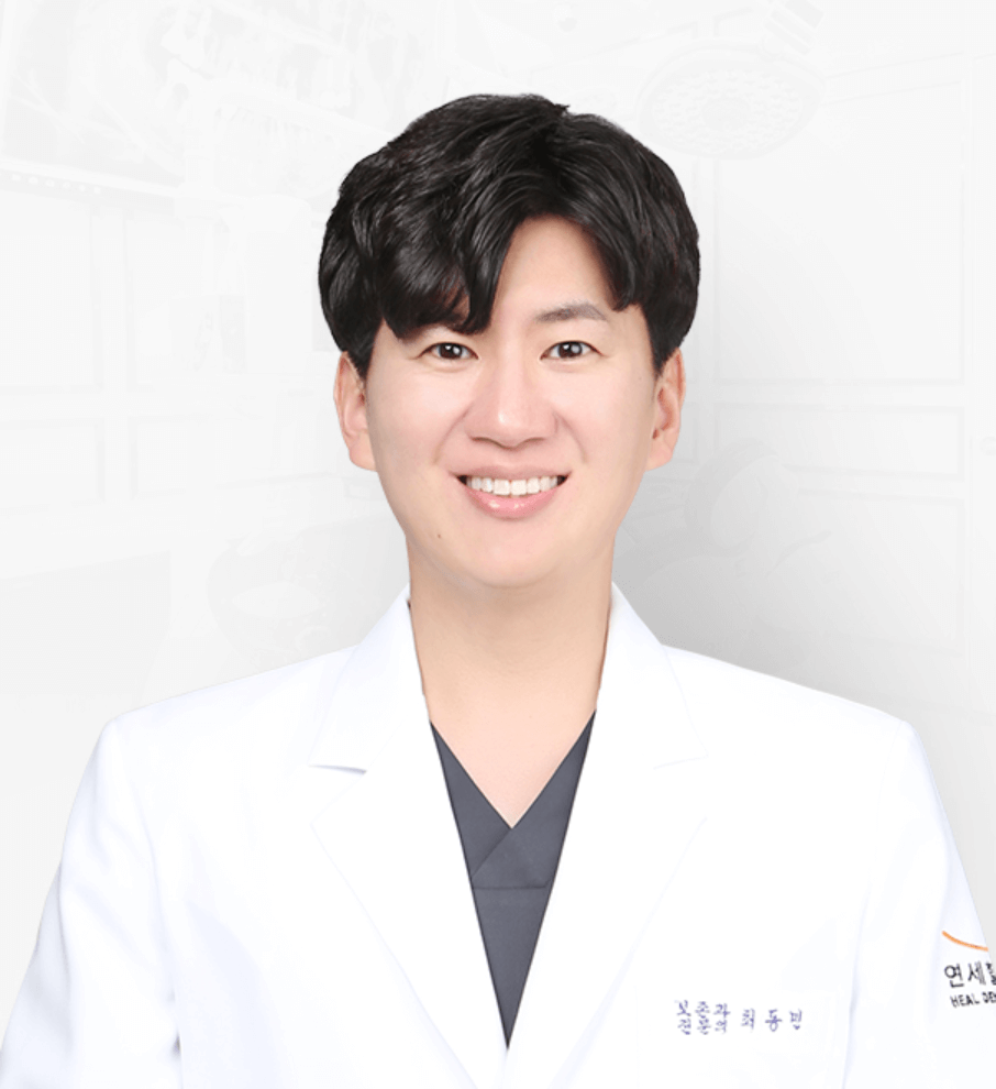 Smiling man in a white coat, likely a doctor, against a blurred white background.