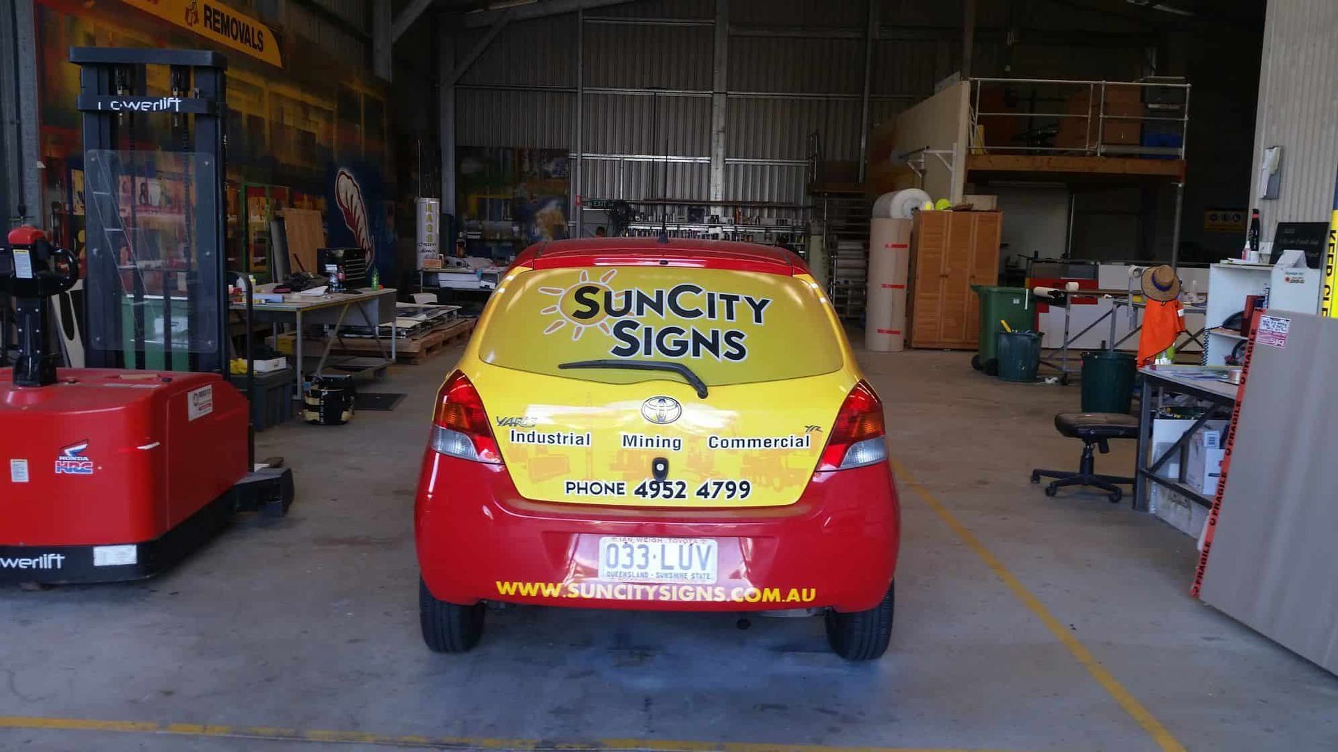 A Red And Yellow Car Is Parked In A Warehouse — Sun City Signs In Paget, QLD
