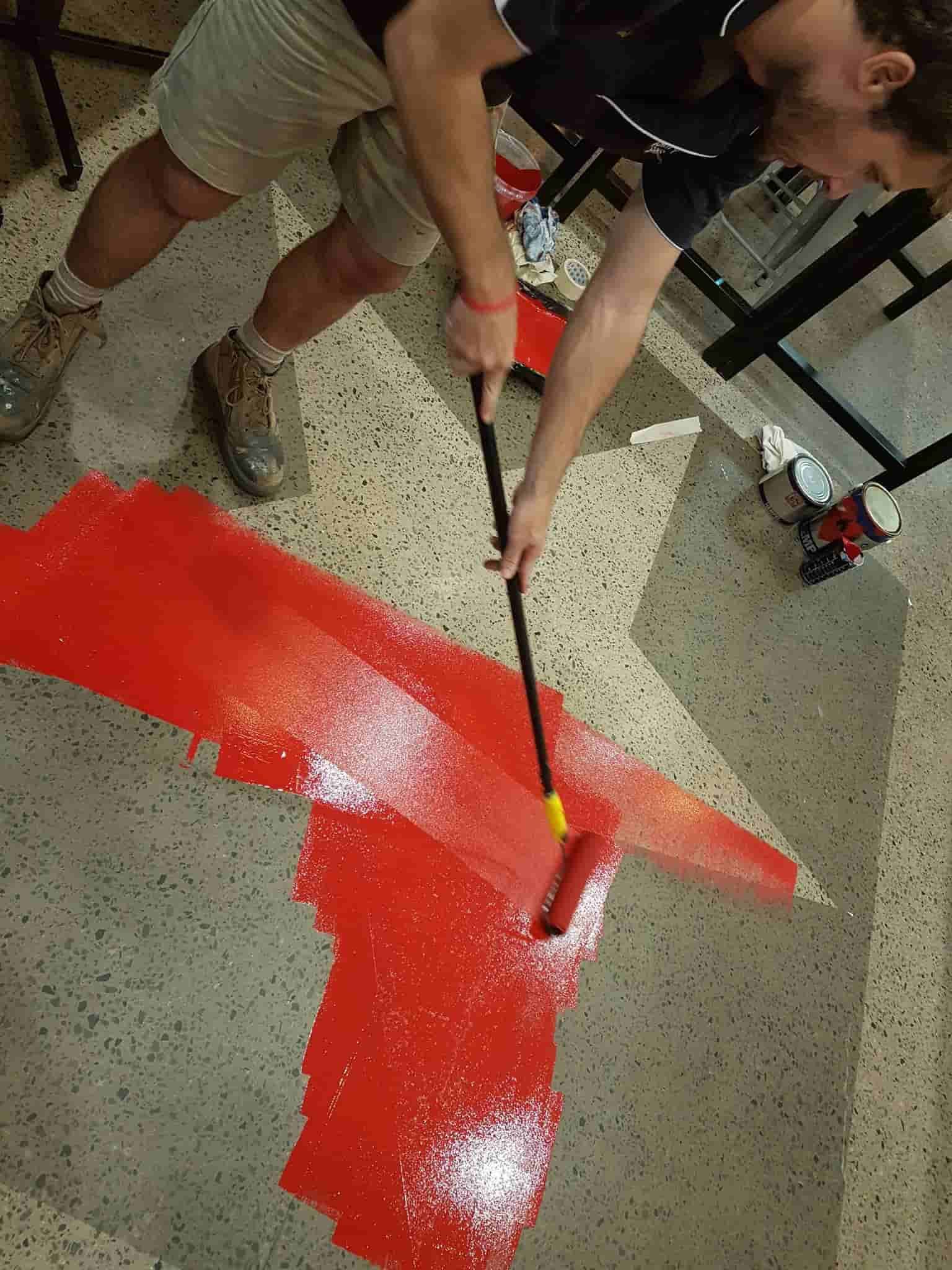 A Man Is Painting A Red Arrow On The Floor With A Roller — Sun City Signs In Dysart, QLD