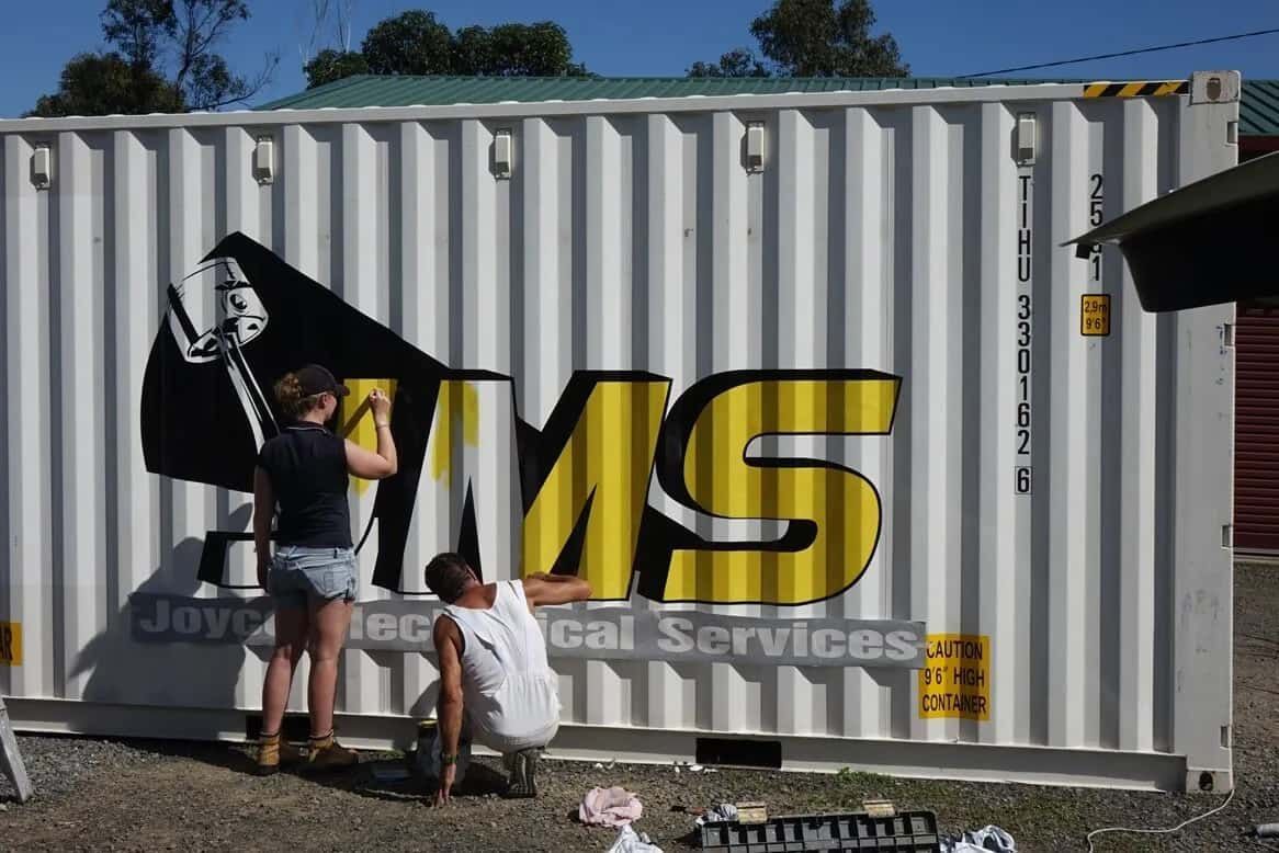 Two People Are Painting A Shipping Container With The Word Ms On It — Sun City Signs In Paget, QLD