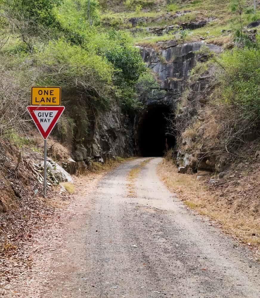 A Dirt Road Leading To A Tunnel With A Yellow Sign That Says One Lane — Sun City Signs In Paget, QLD