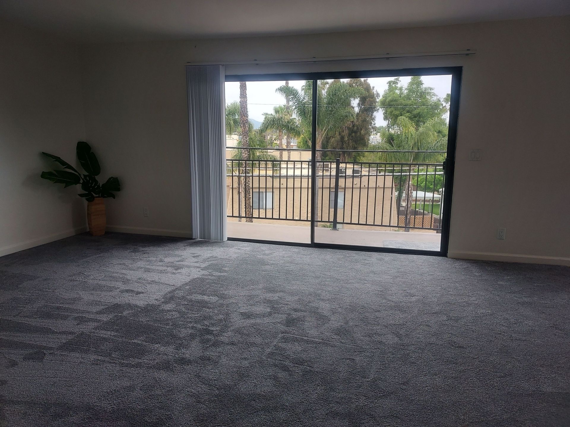 An empty living room with a sliding glass door leading to a balcony.